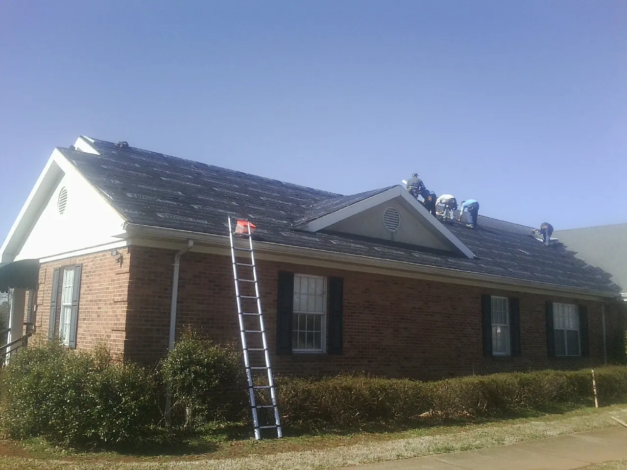 Crew tearing shingles off a brick ranch roof with a ladder set — Metal Roof Repair work by our crew in Brooktondale