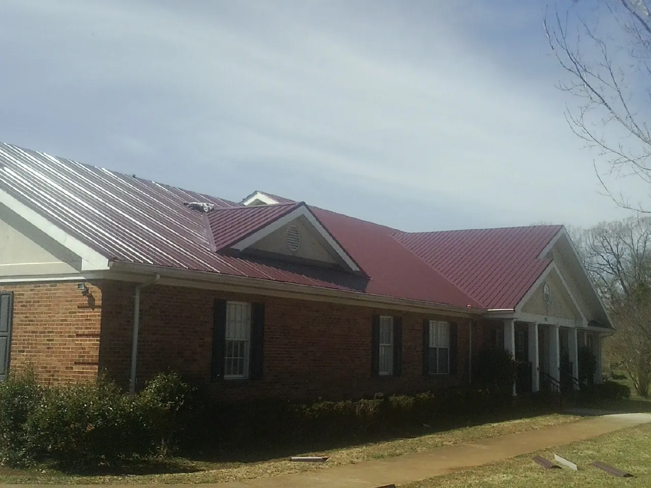 Red metal roof with gabled entries on a long brick building, from a Hail Damage Roof Repair job in Brooktondale