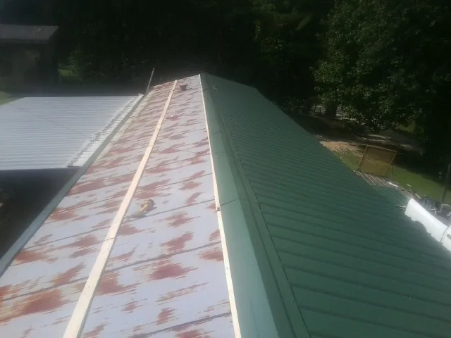 Old rusted panels beside newly installed green metal roofing — Wind Damage Roof Repair by Roofing Brothers in Brooktondale