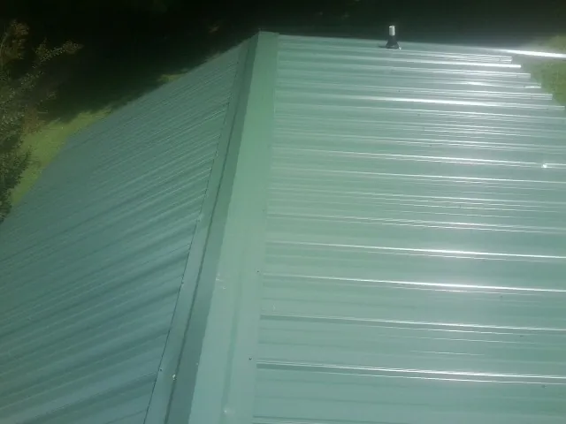 New green metal panels meeting at the ridge of a roof — Flat Roof Repair work by our crew in Brooktondale