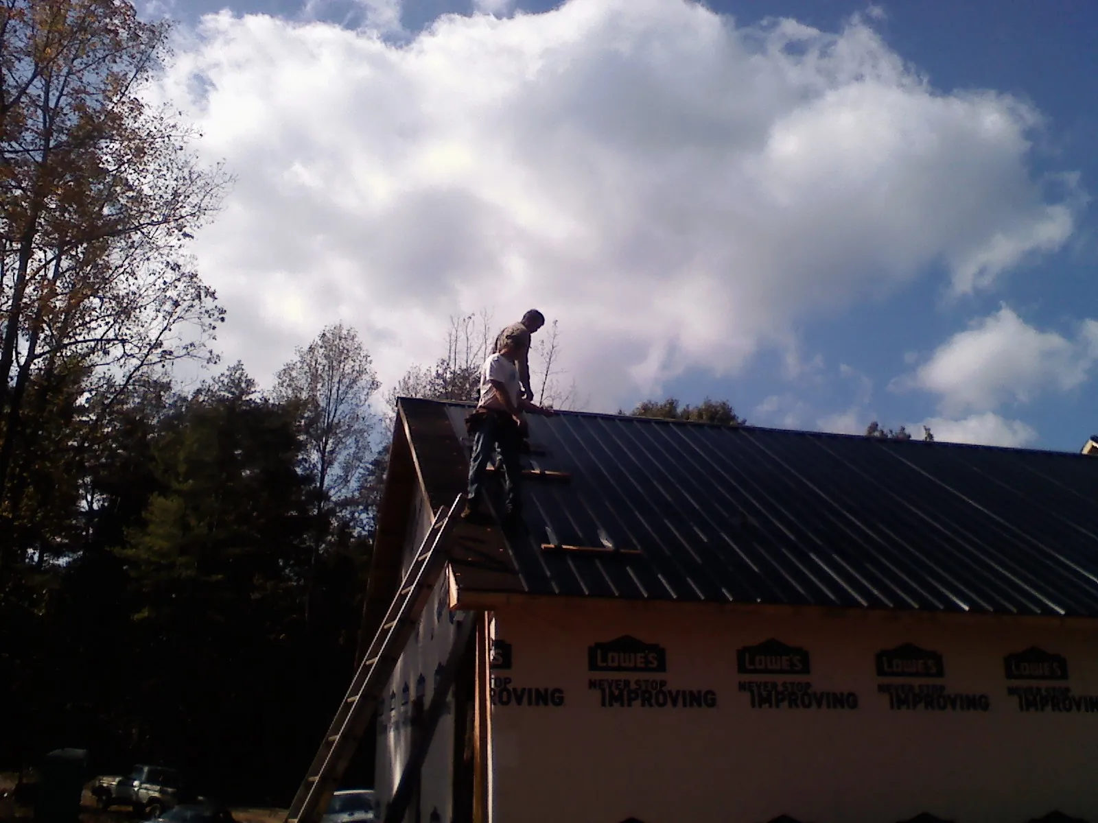 Roofer fastening dark metal panels high against a cloudy sky, from a Roof Inspection job in Brooktondale