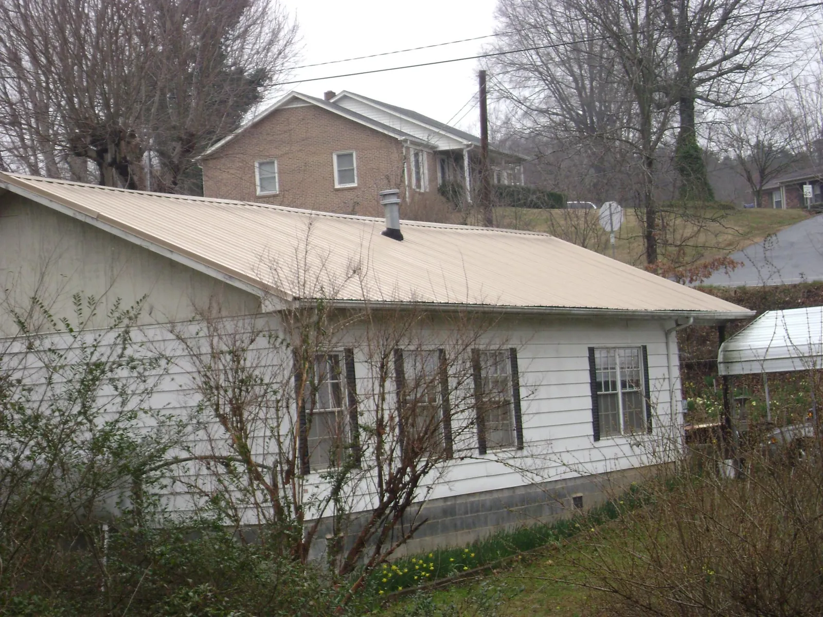 Tan metal roof on a white sided house set into a hillside — Commercial Roofing by Roofing Brothers in Brooktondale