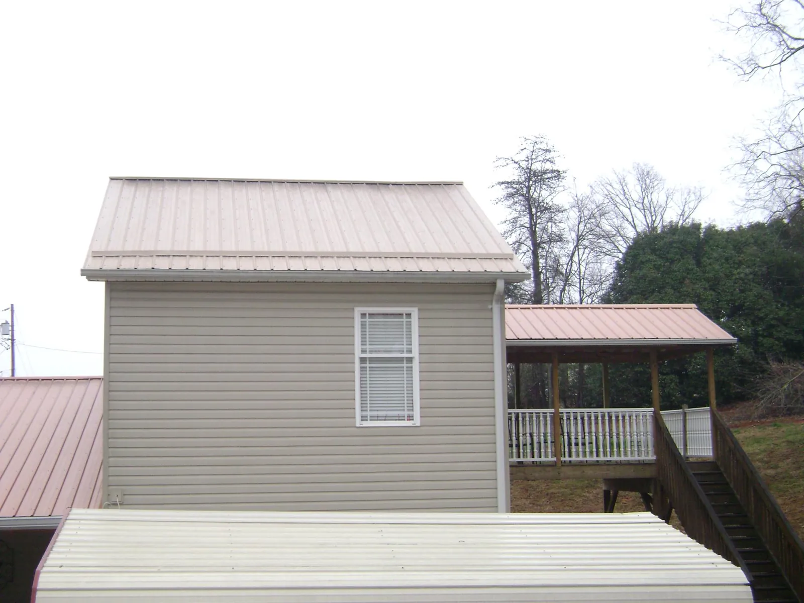 Tan metal roofs on a two story addition and attached porch, from a Roof Replacement job in Brooktondale